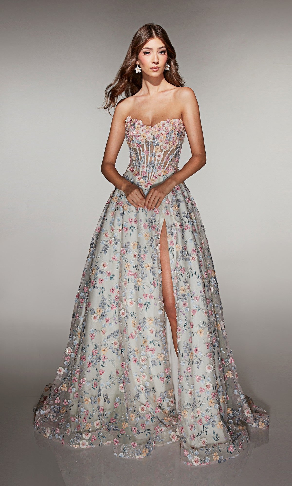 A woman wears the Alyce 61986 long prom dress, featuring a strapless design, 3D floral appliques, sheer bodice, and high slit, standing against a plain background.